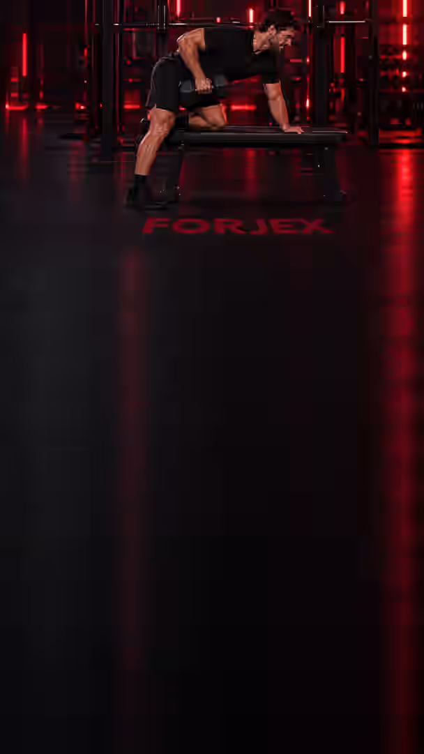 Ein Athlet rudert mit einer Kurzhantel auf einer Bank in einem dunklen Gym, FORJEX steht auf dem Boden.